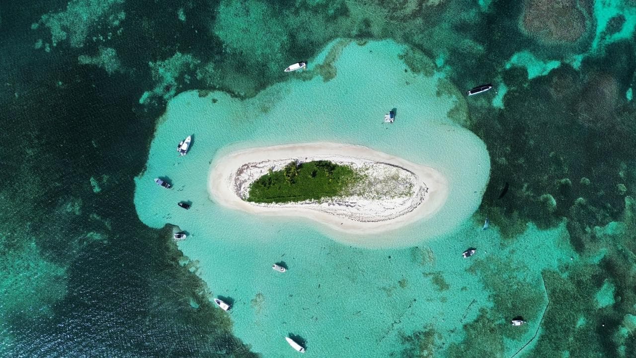 Vue aérienne d’un îlet de sable cerné par le lagon turquoise, les bateaux au mouillage