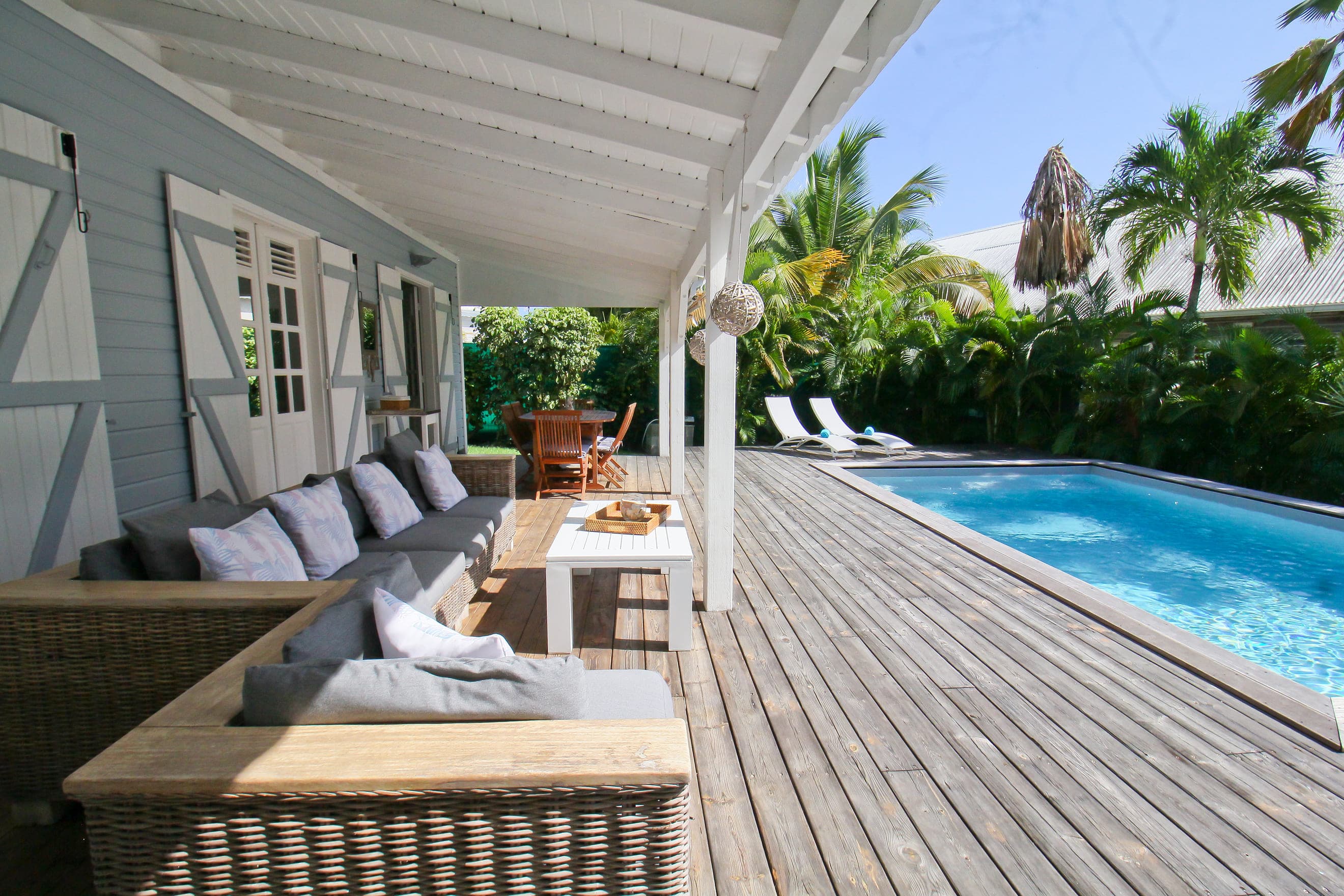 Terrasse en bois de la Villa Alizé le long du bassin, banquette d’extérieur et transats