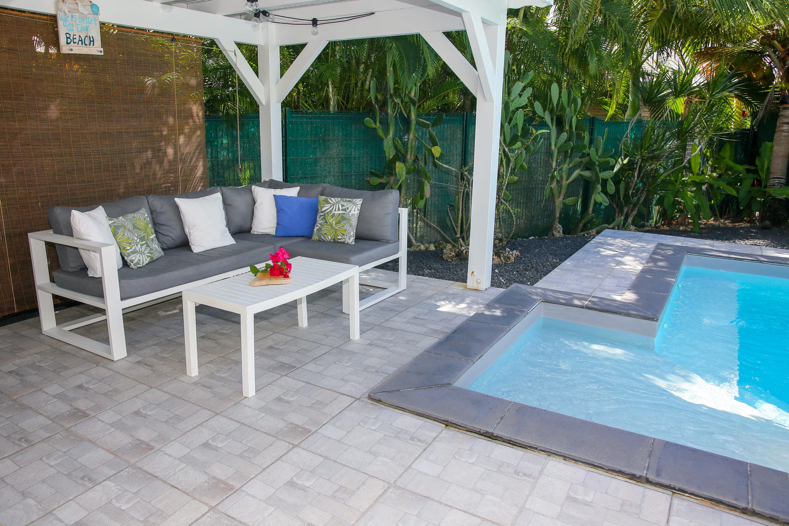 Piscine au sel de la Villa Bahia vue depuis le salon d’extérieur, bains de soleil et haie de palmiers