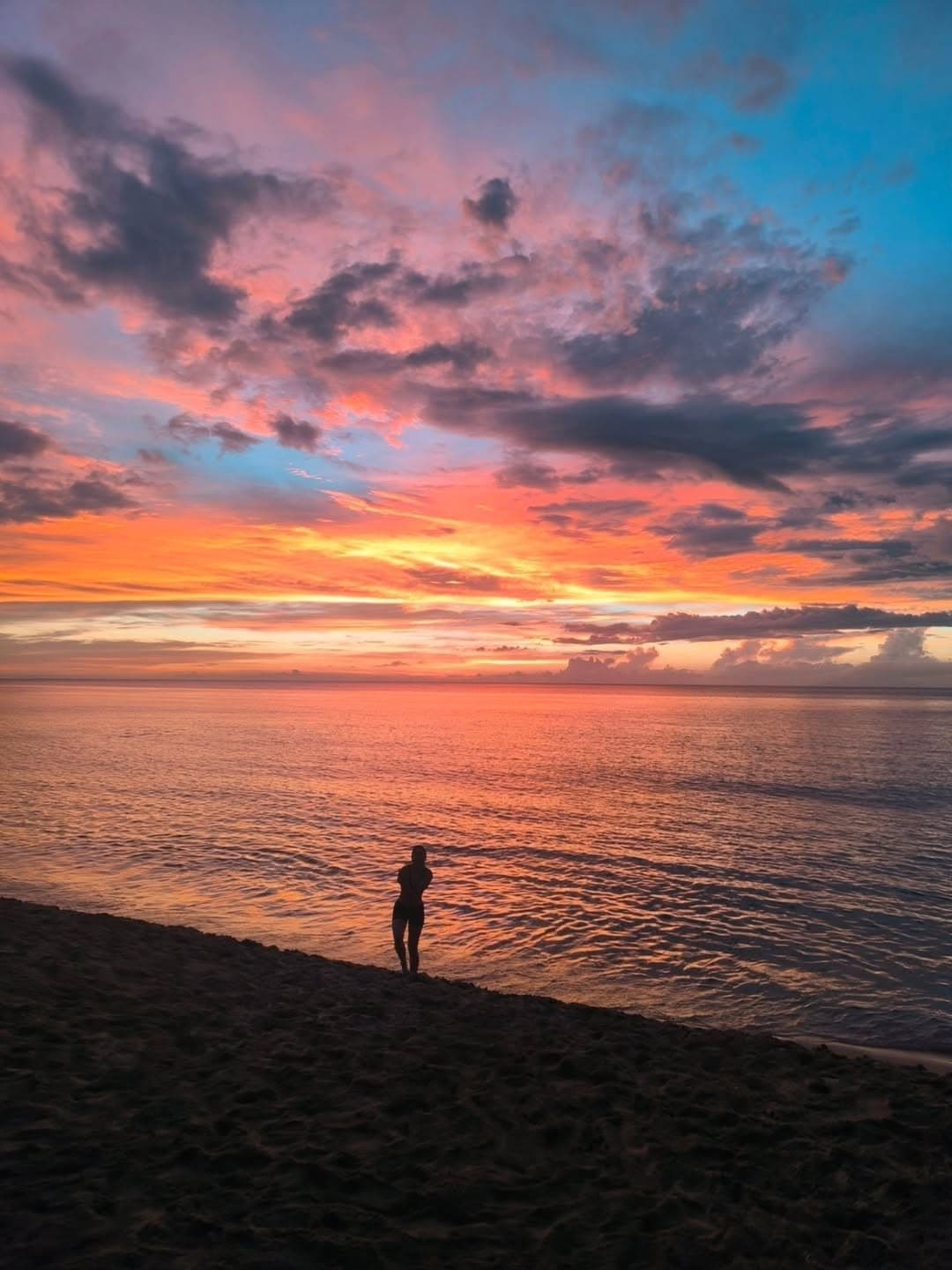 Coucher de soleil rose et orangé sur la mer, une silhouette au bord de l’eau